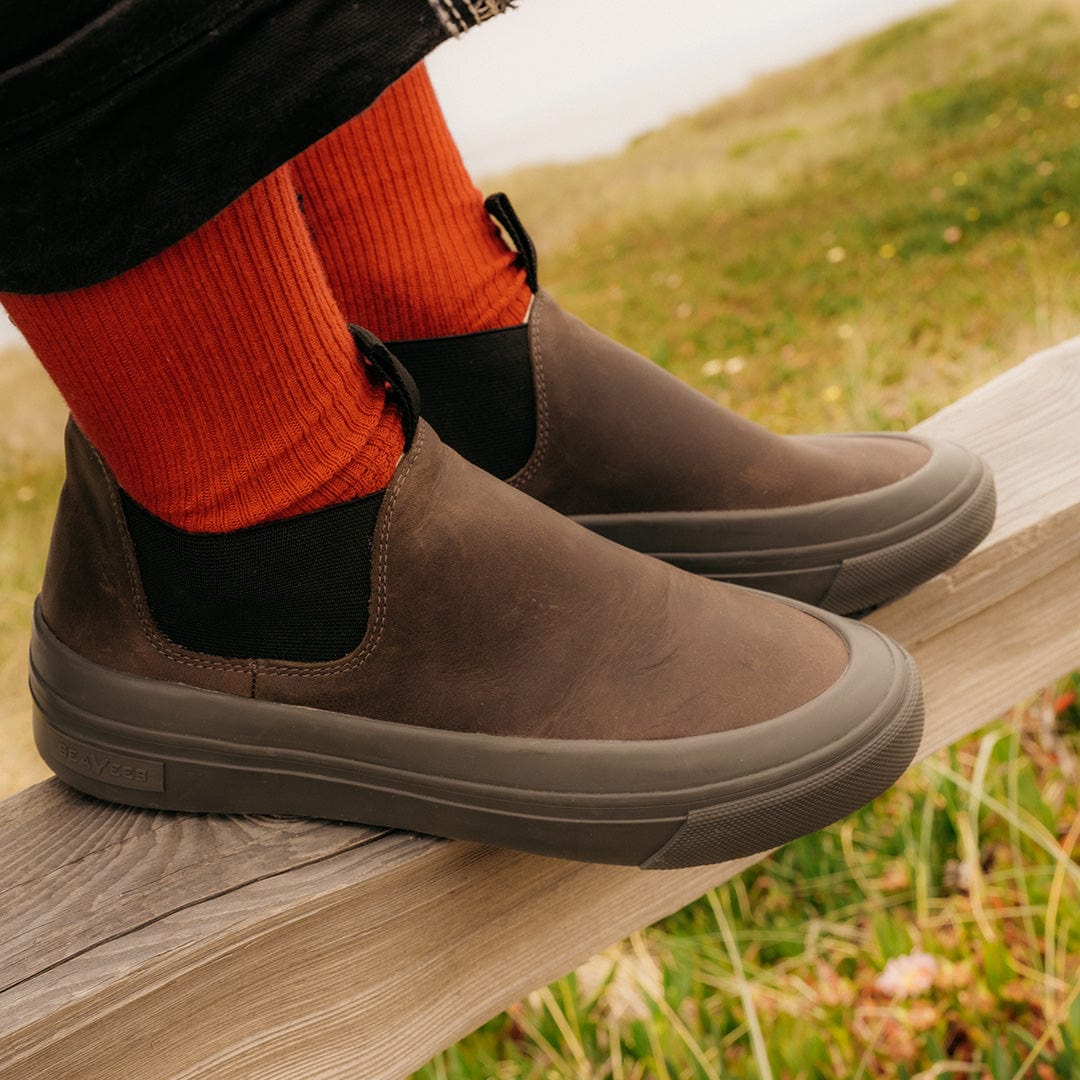 Person sitting on a wooden fence wearing Ballard Boots in Charcoal with red socks.