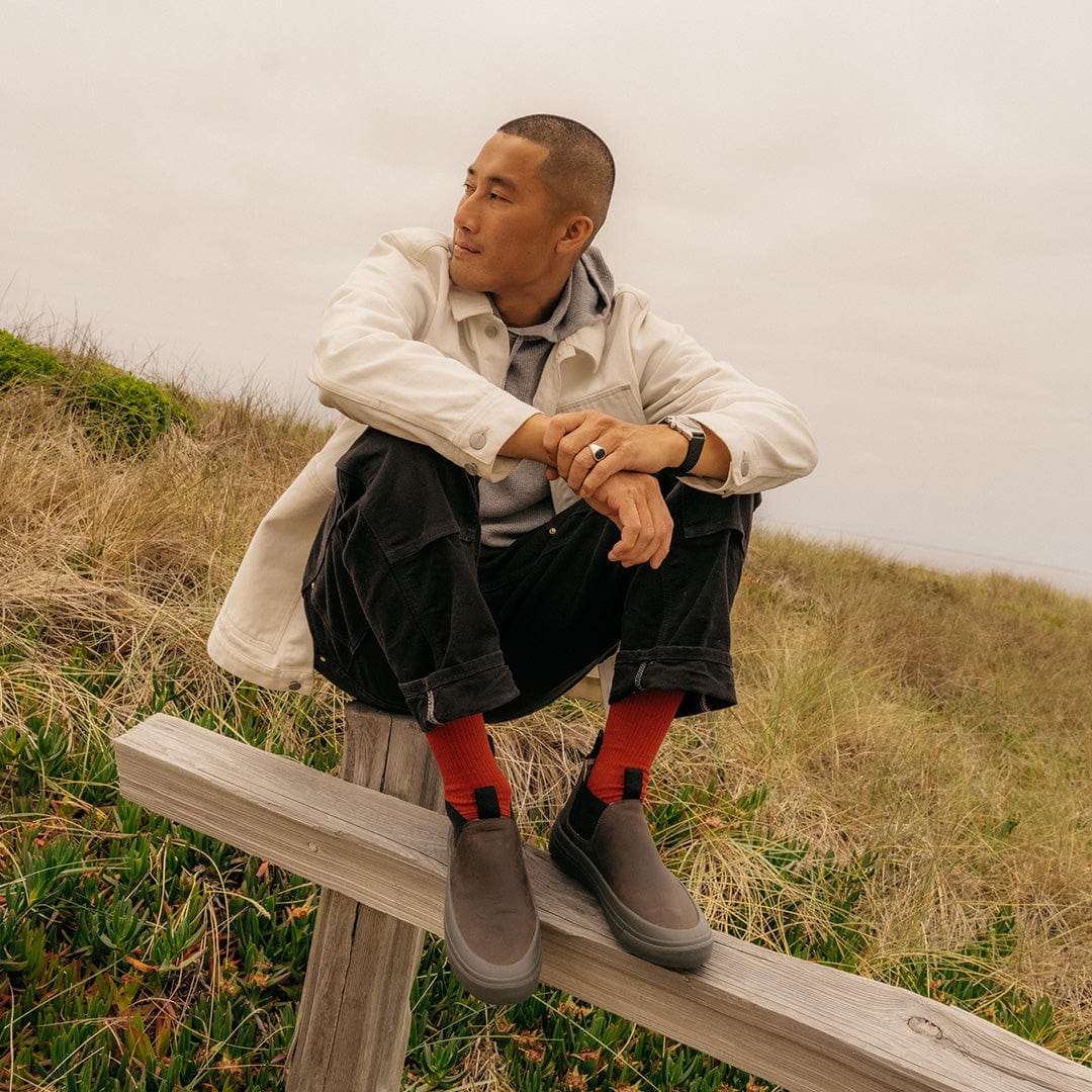 Casual outdoor image of a person wearing Ballard Boots in Charcoal, seated in a field.