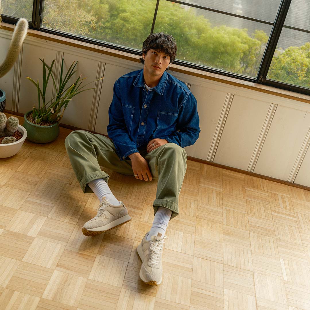 Lifestyle shot of a person wearing the Acorn Trainer in the Color cloud, sitting on a hardwood floor.