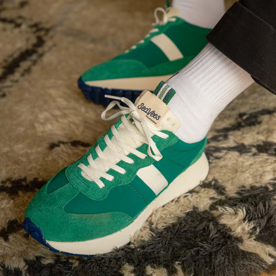 A close up lifestyle shot of the Acorn sneaker in Grass Green, showing the white laces and branding.