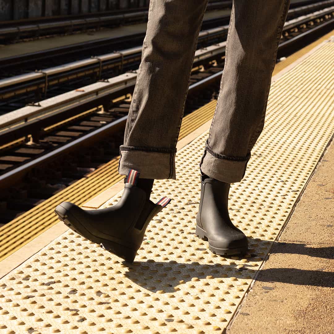 Person standing on train platform wearing Bolinas Off Shore Boots in Black with rolled-up jeans.