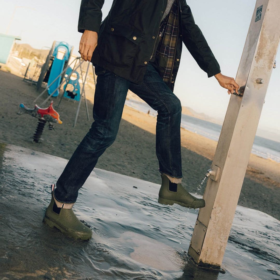 Person by the beach in Bolinas Off Shore Boots in Military Olive, near a shower post.