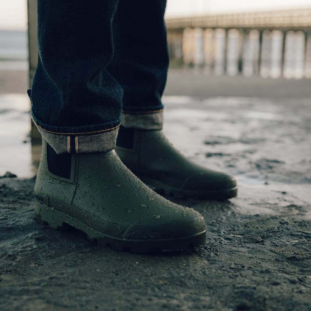 Close-up of feet in Bolinas Off Shore Boots in Military Olive on wet sandy beach.