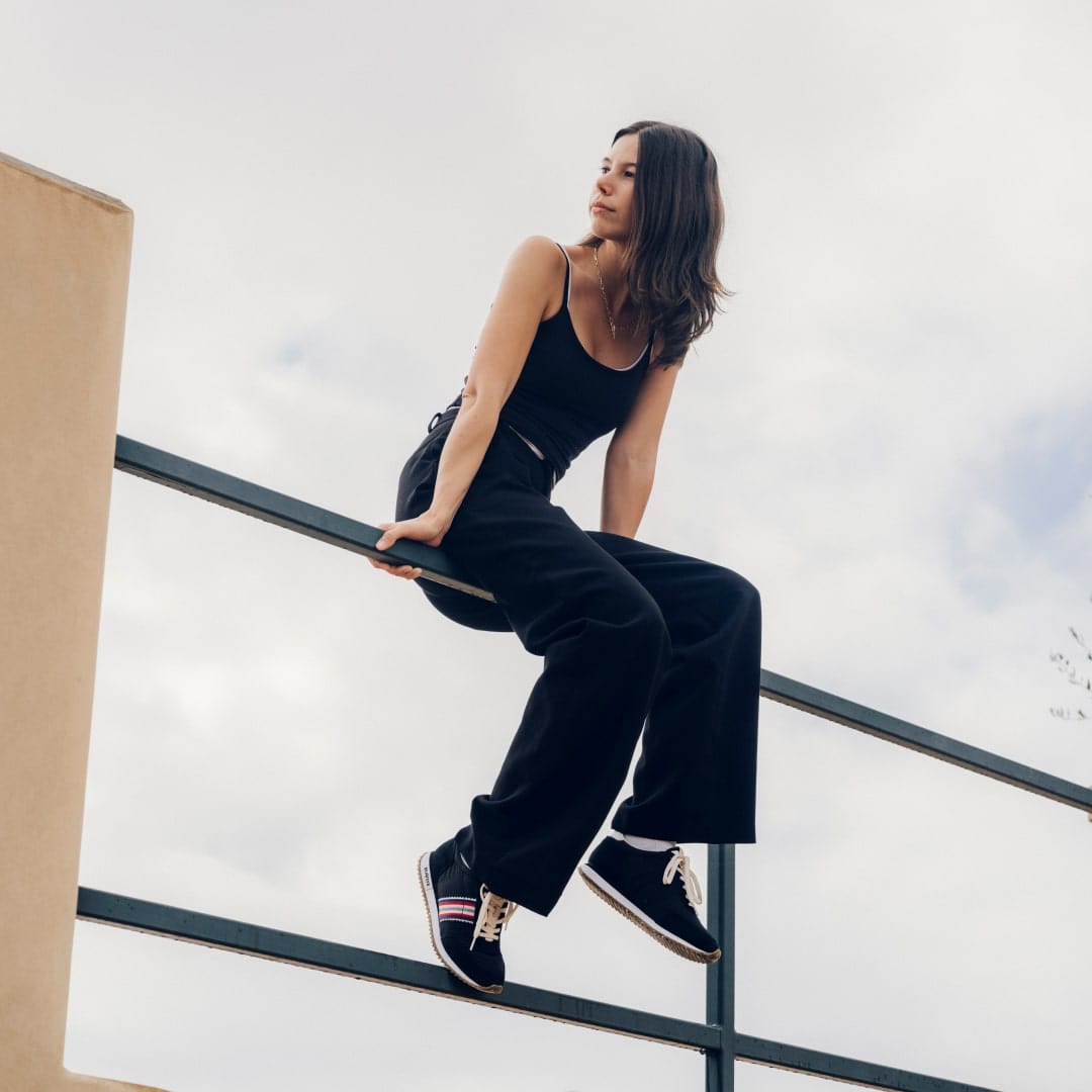 Angled-up view of someone sitting on a railing wearing a black outfit with the Royal Runner Sneaker in Black.