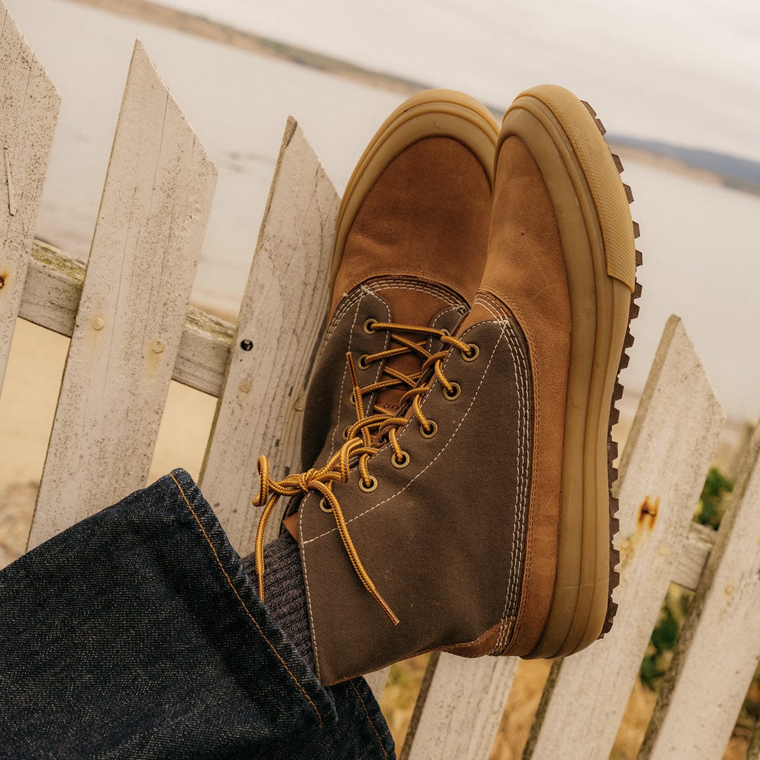Casual style with Cascade Range boots in Cashew/Olive, crossed legs resting on a wooden fence by the seaside.