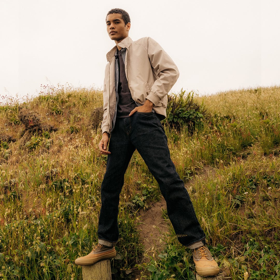 Man in a light jacket and jeans standing confidently in a grassy field, wearing Cascade Range boots in Cashew/Olive.