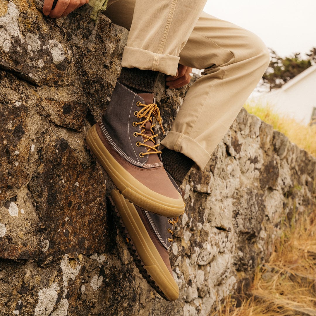 A close-up of Hickory/Charcoal Cascade Range Boots worn with rolled-up trousers, resting on a rocky outcrop.