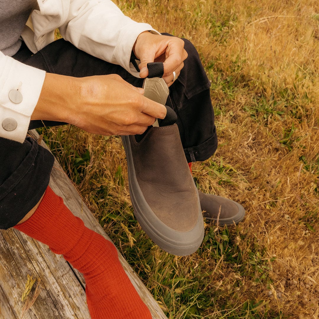 Close-up of a hand pulling on the tab of a Ballard Boot in Charcoal while outdoors.