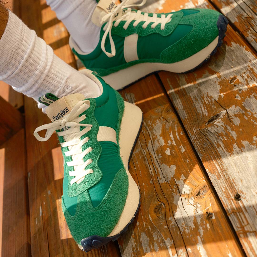 A close-up shot of a person wearing the Acorn in Grass Green standing on a wooden deck.