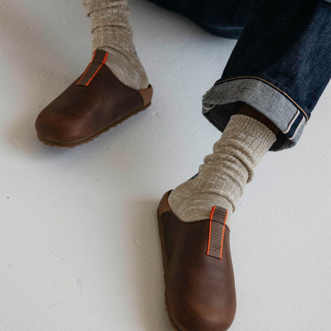 Men's Tiburon Trekker sandal in Elmwood leather, worn with rolled jeans and gray socks on a white floor