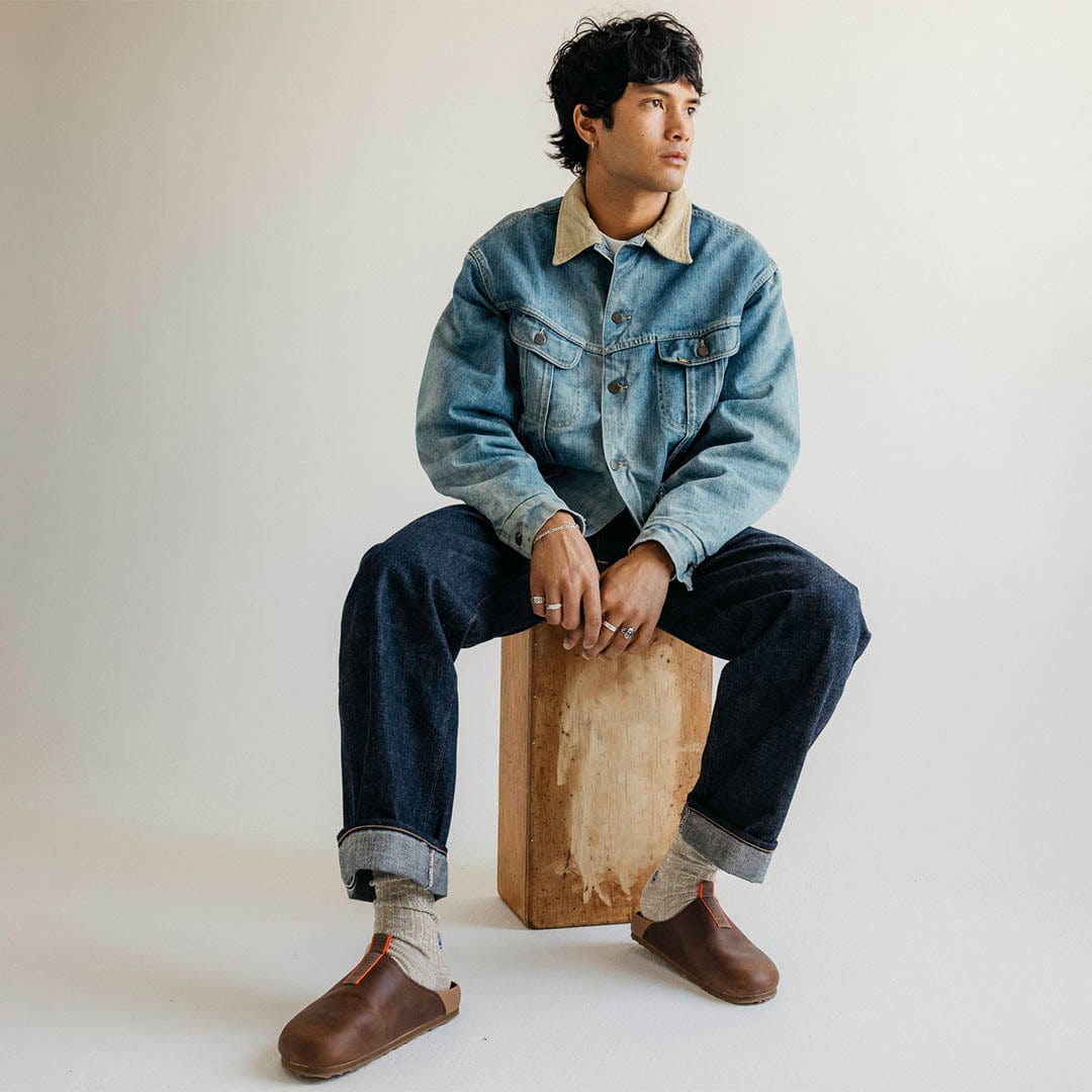 Men's Tiburon Trekker sandal in Elmwood leather, worn by a person seated on a wooden block in a denim jacket