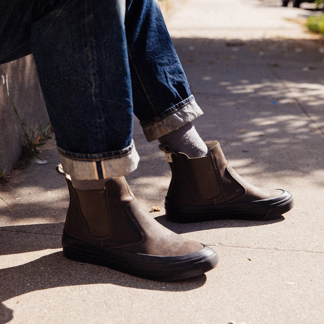 Person standing on sidewalk in cuffed jeans and Beyond & Back Boots in Black Olive, showcasing side profile and pull tab detail.