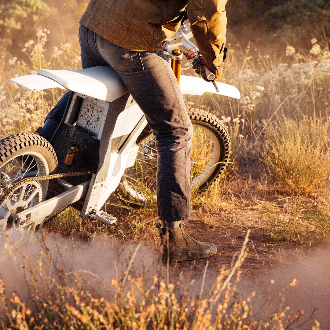 Rider in Beyond & Back Boots in Black Olive, pausing on a dirt trail with a motorcycle, emphasizing the boot's rugged design.