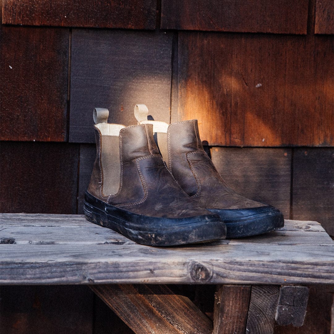 Worn Beyond & Back Boots in Black Olive placed on a rustic wooden table, highlighting their durability and lived-in appeal.