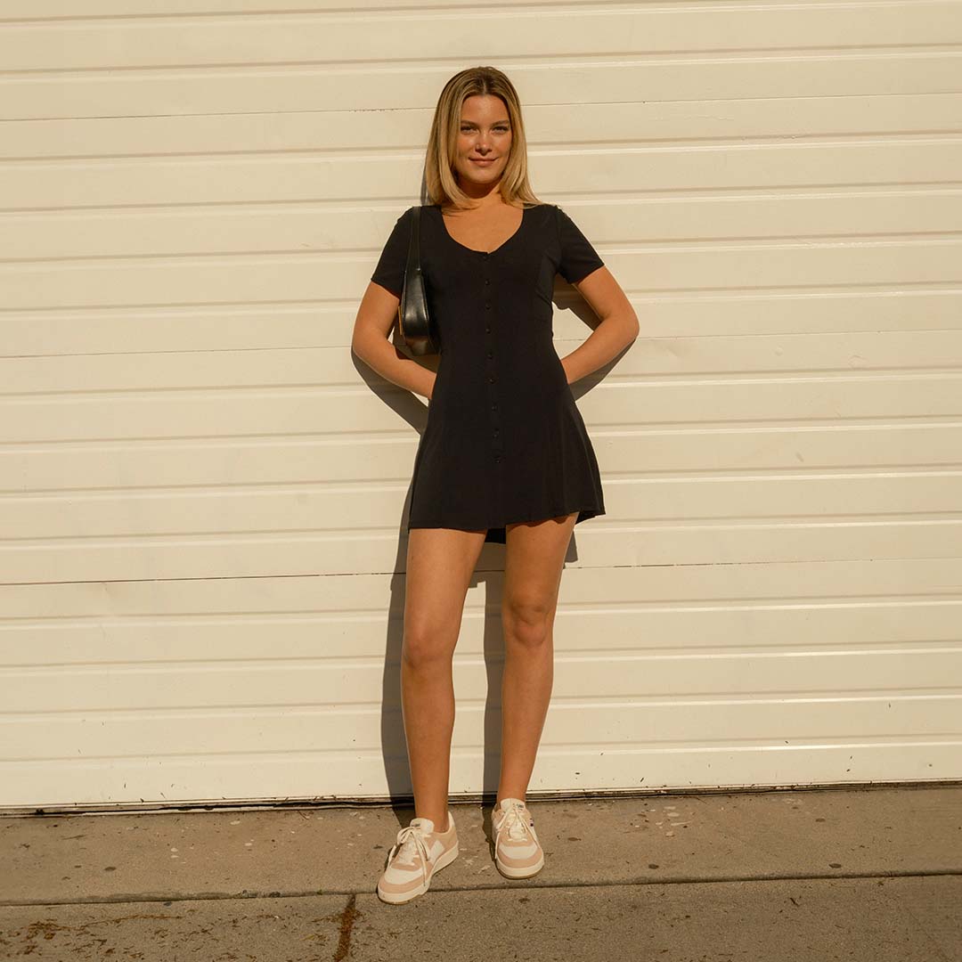 Person standing against a white wall wearing an all black outfit with the Cardinal Sneaker in Pink Sand