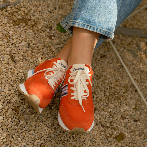 Close-up view of feet wearing Royal Runner sneakers in Strawberry, featuring logo on tongue and white laces.