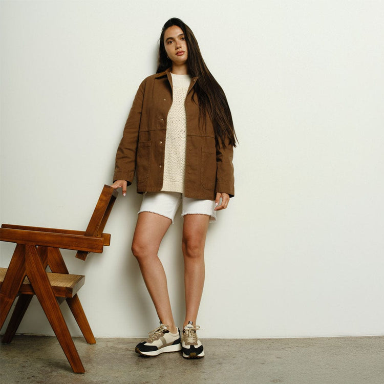 Women's Acorn Trainer sneaker in Black and Tan nylon and suede, worn by a person standing in a brown jacket and white shorts