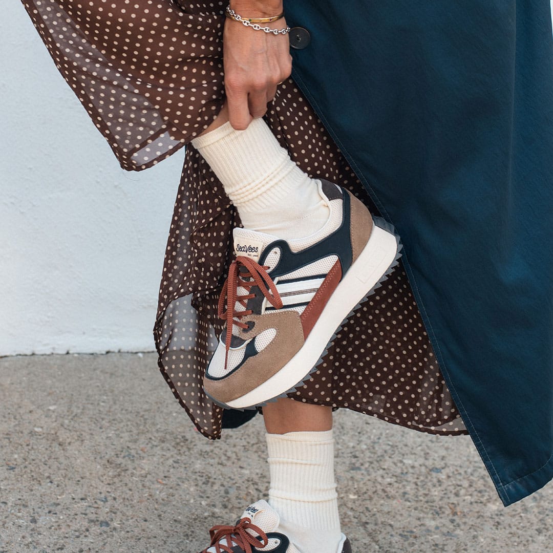 Women's Causeway Trainer sneaker in All Spice mesh and leather, worn with white socks, one foot raised, polka dot skirt
