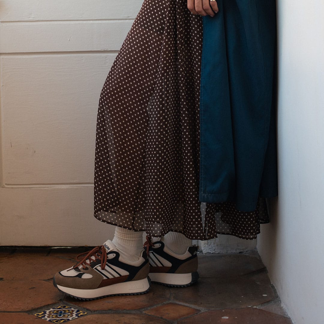 Women's Causeway Trainer sneaker in All Spice mesh and leather, worn with a polka dot skirt and white socks, standing