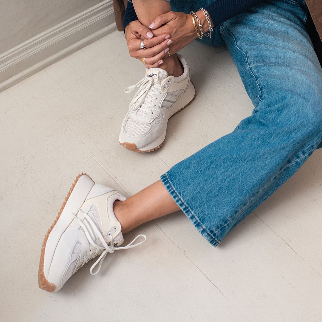 Women's Causeway Trainer sneaker in Cloud mesh and leather, worn with jeans, seated on a white floor