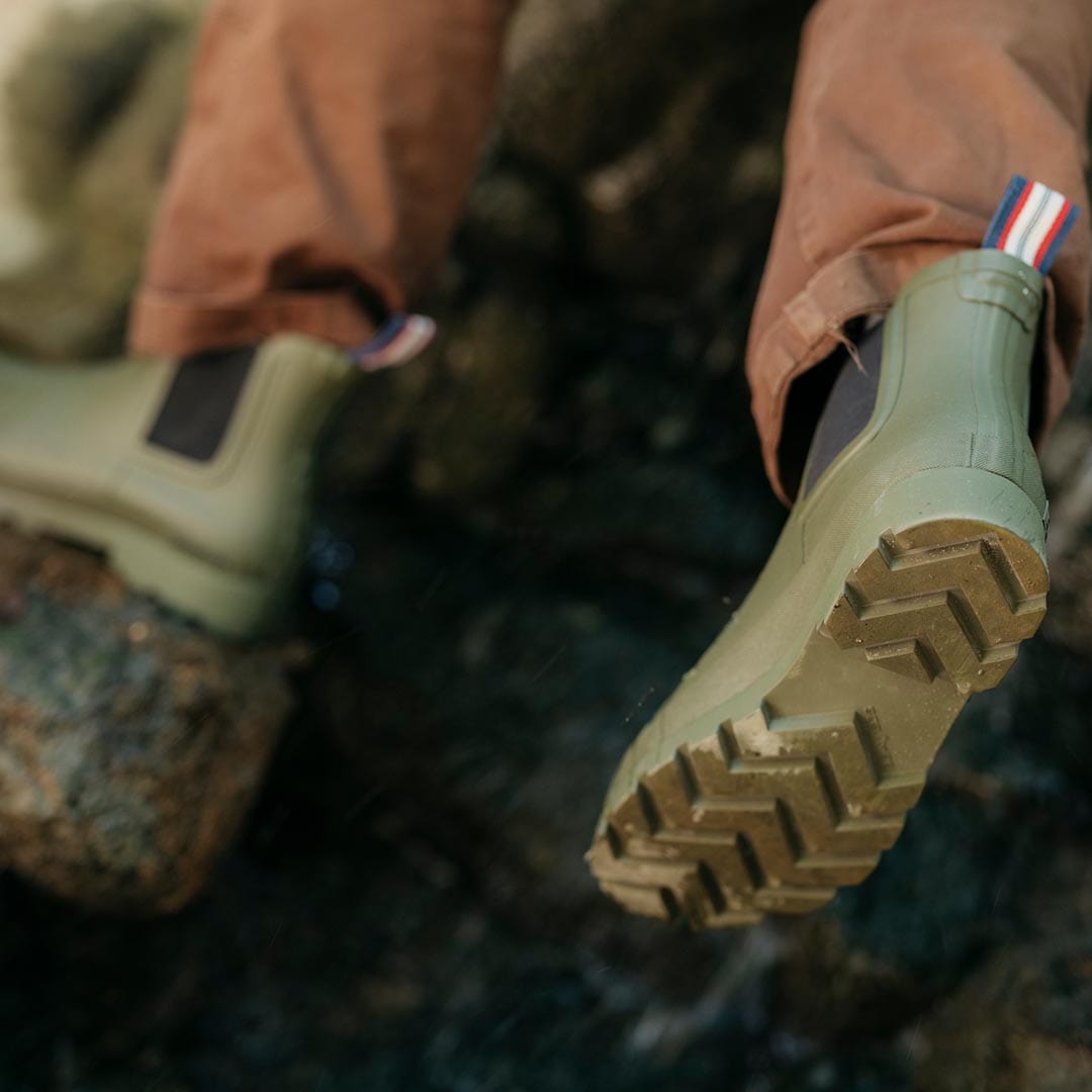 Close-up of Bolinas Off Shore Boot in Military Olive, sole facing the camera on a rocky surface.