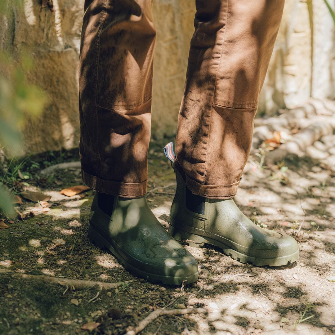Person walking in a wooded area wearing Bolinas Off Shore Boots in Military Olive, side view.