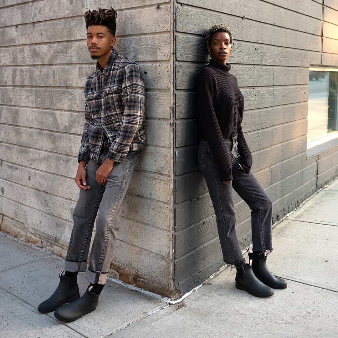 Two people standing against a wall, both wearing Bolinas Off Shore Boots in Black and casual attire.