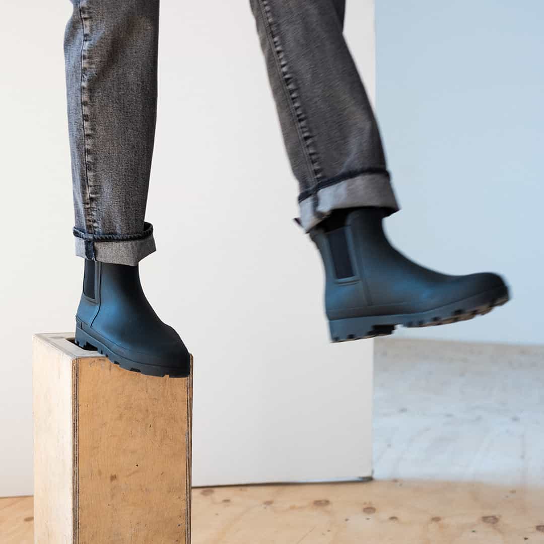 Close-up on feet of person wearing Bolinas Off Shore Boots in Black, standing on wooden box.