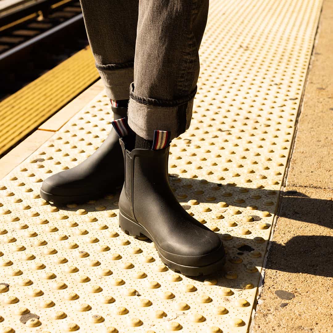 Sunny outdoor setting with person wearing Bolinas Off Shore Boots in Black on a textured walkway.